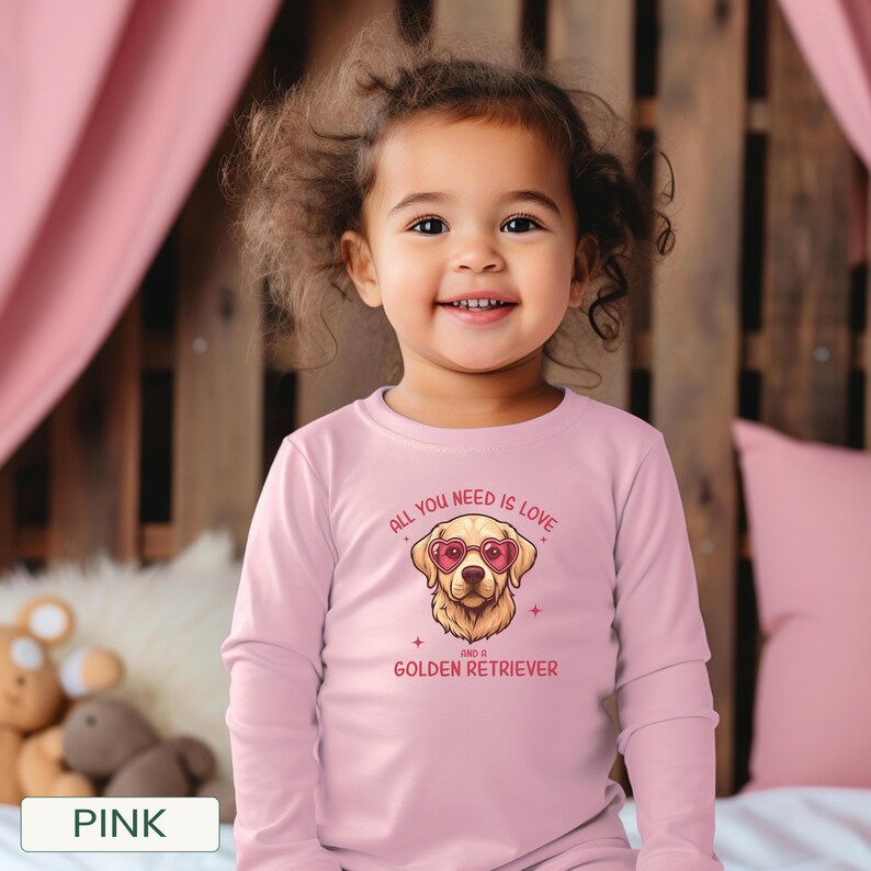 Puede incluir: Una camiseta rosa de manga larga con un Golden Retriever con gafas de sol en forma de coraz&oacute;n. La camiseta tiene el texto "ALL YOU NEED IS LOVE AND A GOLDEN RETRIEVER". La camiseta la lleva un ni&ntilde;o peque&ntilde;o.