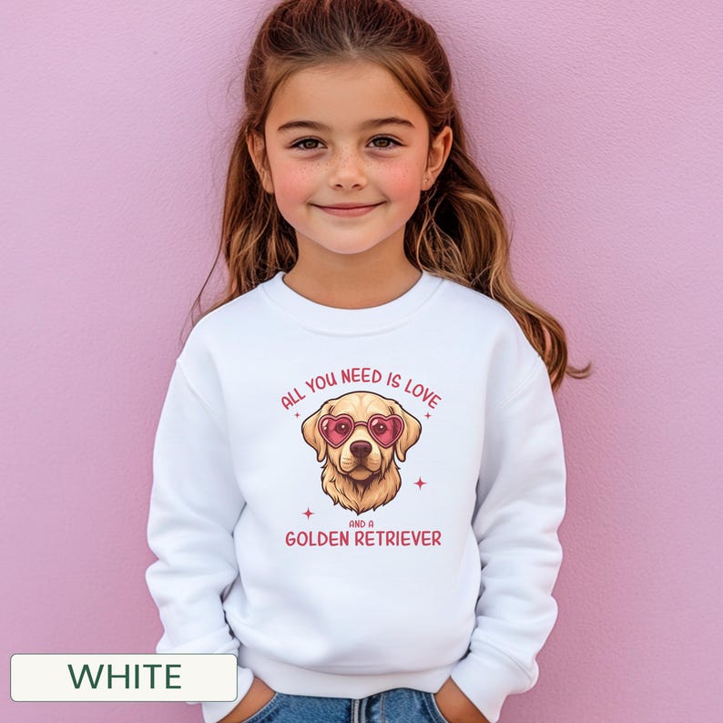 Puede incluir: Sudadera blanca con un dise&ntilde;o de Golden Retriever con gafas de sol en forma de coraz&oacute;n. El texto en rosa dice "ALL YOU NEED IS LOVE AND A GOLDEN RETRIEVER". Llevada por una ni&ntilde;a.