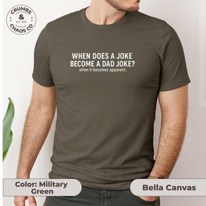 May include: Military green t-shirt with the text "WHEN DOES A JOKE BECOME A DAD JOKE? when it becomes apparent." The shirt is a Bella Canvas brand.