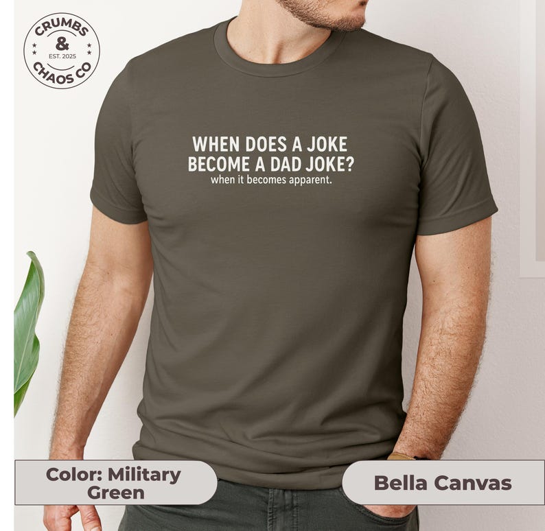 May include: Military green t-shirt with the text "WHEN DOES A JOKE BECOME A DAD JOKE? when it becomes apparent." The shirt is a Bella Canvas brand.