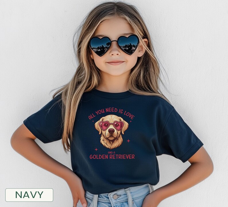 Puede incluir: Camiseta azul marino con un dise&ntilde;o de Golden Retriever con gafas de sol en forma de coraz&oacute;n. El texto "All you need is love and a Golden Retriever" est&aacute; impreso encima y debajo de la ilustraci&oacute;n del perro. La camiseta la lleva una persona.