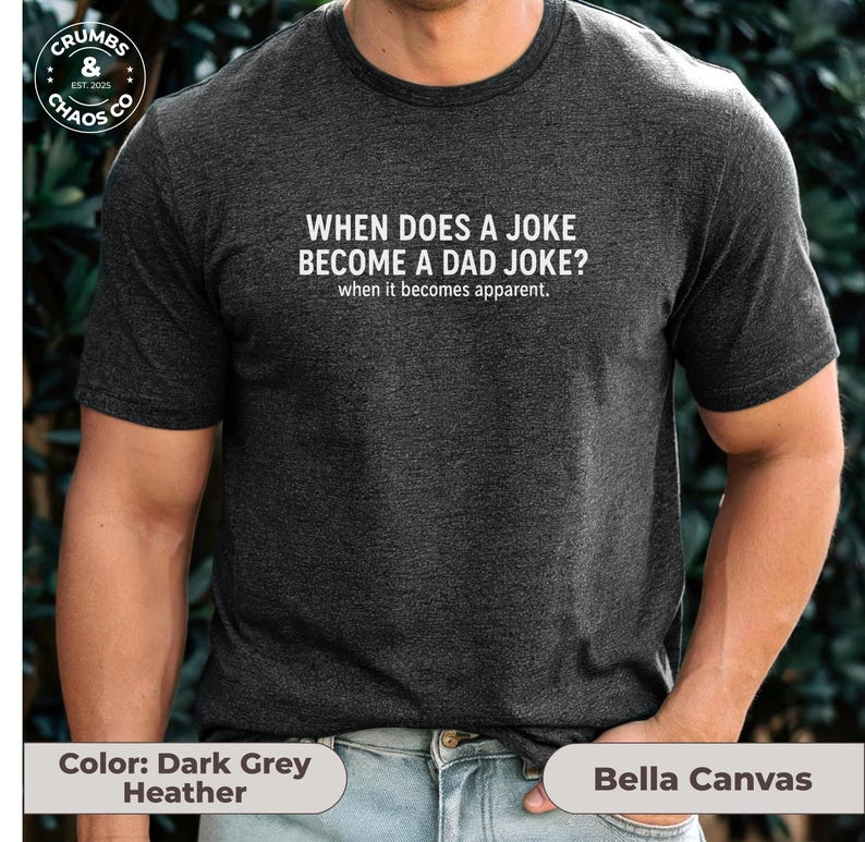 May include: Dark grey heather t-shirt with the text "WHEN DOES A JOKE BECOME A DAD JOKE? when it becomes apparent." The shirt is made by Bella Canvas. The Crumbs & Chaos Co. logo is in the upper left corner.