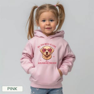 Puede incluir: Una sudadera con capucha rosa con un gr&aacute;fico de un Golden Retriever con gafas de sol en forma de coraz&oacute;n. El texto "ALL YOU NEED IS LOVE AND A GOLDEN RETRIEVER" est&aacute; impreso encima y debajo de la ilustraci&oacute;n del perro. El ni&ntilde;o lleva la sudadera.