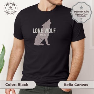 May include: Black t-shirt with a distressed gray wolf graphic and the text "LONE WOLF CLUB". The shirt also has the text "CRUMBS & CHAOS CO EST. 2025" and "Bella Canvas" printed on it. A "Perfect Gift" badge is also visible.