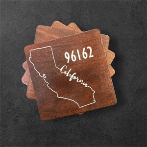 Könnte beinhalten: Holzuntersetzer mit dunkelbraunem Finish. Jeder Untersetzer zeigt eine weiße Umrisslinie des Bundesstaates Kalifornien, das Wort "California" in Schrift und die Postleitzahl 96162.