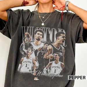May include: Dark gray t-shirt featuring a collage of basketball player images with the name "VICTOR" and "Wembanyama" printed on it. The shirt has a vintage, distressed look with a "PEPPER" label.