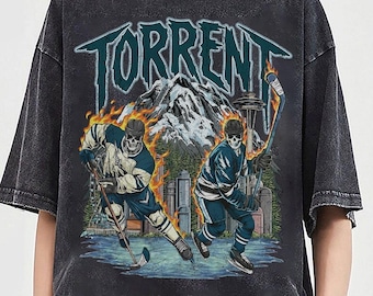May include: Dark gray t-shirt with a graphic featuring the word "TORRENT" above two skeleton hockey players on a rink with a mountain and city skyline backdrop. The design includes flames and a teal and white color scheme.