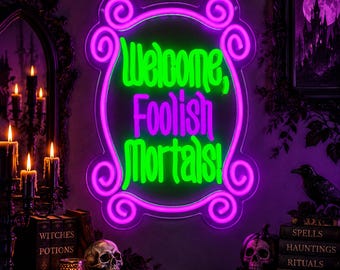 Könnte beinhalten: Ein Neonschild mit einem leuchtend pinkfarbenen, geschwungenen Rahmen und dem Text "Welcome, Foolish Mortals!" in leuchtend grüner Schrift. Das Schild ist auf einer transparenten Acrylplatte montiert und strahlt ein helles Licht aus.
