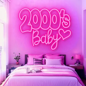 Pode incluir: Um quarto rosa com uma cama, mesinhas de cabeceira e uma placa de n&eacute;on que diz "2000's Baby" acima da cama. A cama tem roupa de cama e almofadas rosa. Uma pequena planta est&aacute; na mesinha de cabeceira. O quarto &eacute; pintado de rosa.