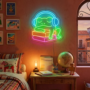 May include: A neon sign featuring a green frog wearing blue headphones and resting on a stack of two books. The frog is outlined in bright neon light, with the top book in yellow and the bottom book in pink, mounted on a wall above a wooden desk.