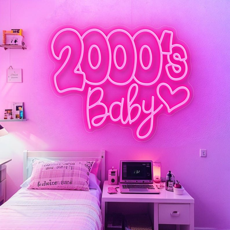 Pode incluir: Uma placa de n&eacute;on rosa que diz "2000's Baby" com um cora&ccedil;&atilde;o, montada numa parede rosa. O quarto apresenta uma cama com uma almofada rosa, uma secret&aacute;ria com um laptop e outros itens decorativos, tudo banhado em luz rosa.