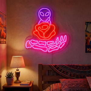 May include: A neon sign featuring a purple alien head silhouette positioned above a bright red rose, which is being held by a skeletal hand outlined in pink neon. The design glows against a textured wall, creating a vibrant light display.