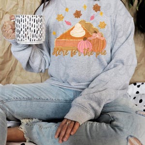 Peut inclure: Un sweat-shirt gris avec un motif de tarte &agrave; la citrouille et le texte "Here for the pie".