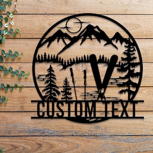 May include: Black metal silhouette of a mountain range with two ski poles and two skis, with the text "CUSTOM TEXT" below. The design is on a wooden background.