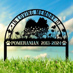 May include: Black metal garden memorial arch with a silhouette of a Pomeranian dog surrounded by flowers. The arch has the text "In Loving Memory Of" at the top and "Pomeranian 2013-2024" at the bottom.