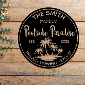 May include: Black and brown round wooden sign with the text "The Smith Family Poolside Paradise Est. 2022 Relax - Unwind - Enjoy" and a silhouette of palm trees.