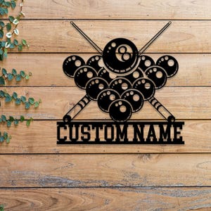 May include: Black metal wall art featuring a group of billiard balls with crossed pool cues and a personalized nameplate that reads "CUSTOM NAME".