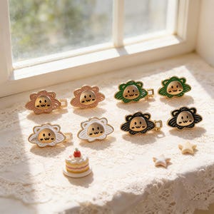 May include: A collection of small, decorative hair clips in various colors, including gold, pink, green, white, and black. Each clip features a lion face design with a flower-shaped mane. Also included are a small cake and star-shaped decorations.