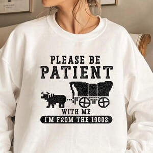 May include: White sweatshirt with black text that reads "Please be patient with me I'm from the 1900s". The text is surrounded by a black and white pixelated image of a horse-drawn wagon.