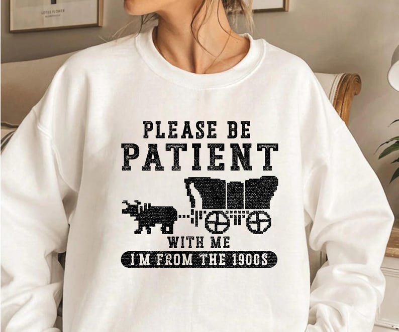 May include: White sweatshirt with black text that reads "Please be patient with me I'm from the 1900s". The text is surrounded by a black and white pixelated image of a horse-drawn wagon.