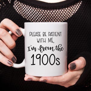 May include: White ceramic mug with black text that reads "Please be patient with me, I'm from the 1900s".