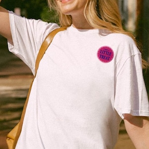 May include: A white t-shirt with a pink circle and the text "Little Treat" in blue letters.