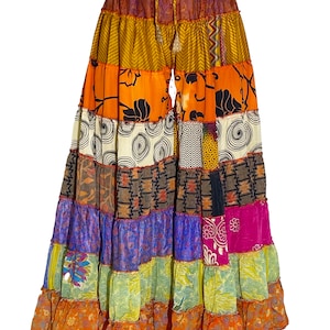 May include: A long, multi-coloured patchwork skirt with a drawstring waist. The skirt is made of various fabrics with different patterns, including floral, geometric, and abstract designs. The skirt is a vibrant mix of orange, yellow, brown, purple, and green.
