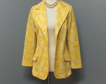 May include: A yellow blazer with a white geometric pattern. The blazer is on a mannequin wearing a pearl necklace.