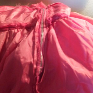 May include: A pink satin garment with a zipper down the center back. The zipper is silver and the fabric is smooth and shiny.