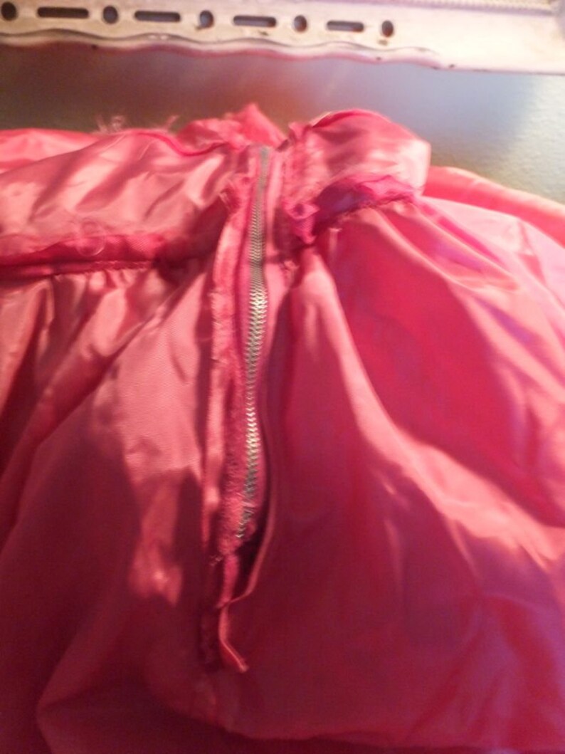 May include: A pink satin garment with a zipper down the center back. The zipper is silver and the fabric is smooth and shiny.