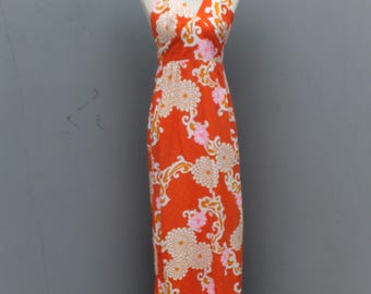 May include: A vintage orange halter maxi dress with a floral pattern in white, pink, and gold. The dress is displayed on a mannequin with a pearl necklace. The dress has a fitted bodice and a flowing skirt.