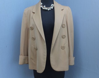 May include: A tan blazer with a double breasted closure and long sleeves. The blazer has a pocket on the left side and is on a black mannequin.