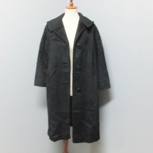 May include: A long black coat with a collar and button closure. The coat is on a wooden mannequin.