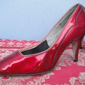 May include: A pair of red patent leather high heels with a pointed toe and stiletto heels.