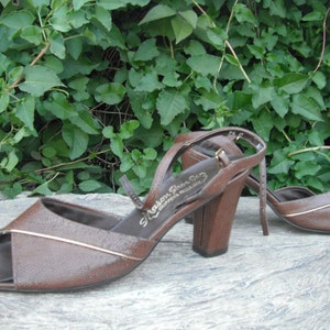 May include: A pair of brown leather heeled sandals with a gold trim. The sandals have a peep toe and an ankle strap. The brand name "Mason Shoe Co." is printed on the insole.