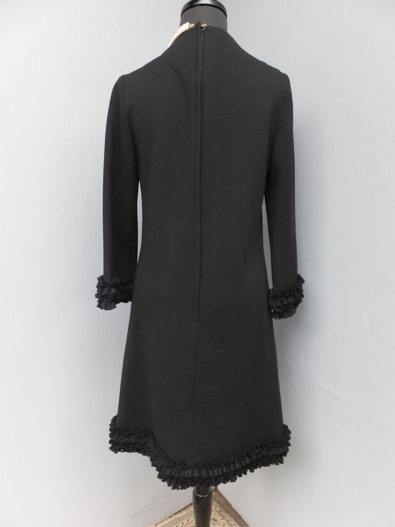 Puede incluir: Un vestido negro con un dobladillo y mangas con volantes. El vestido tiene un dise&ntilde;o simple y elegante y es perfecto para una ocasi&oacute;n especial.