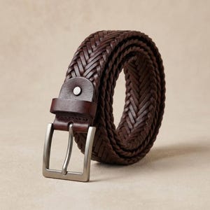 Handmade braided brown leather belt with woven genuine leather texture and metal buckle, artisan handcrafted casual belt for men and women displayed on neutral background, visible leather craftsmanship details