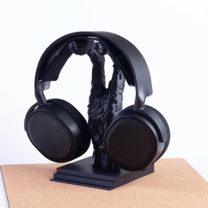 May include: Black wireless headphones with a black stand. The headphones have a large, round earcup design.