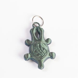 May include: A green turtle keyring with a detailed design and a silver metal ring.