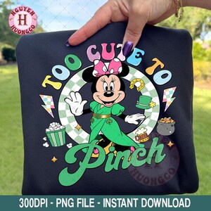 May include: Black sweatshirt featuring a Minnie Mouse graphic in a green St. Patrick's Day outfit. The design includes the text "Too Cute to Pinch" in green, along with shamrocks, a pot of gold, and a beer mug. The design is surrounded by a green and white checkered pattern.
