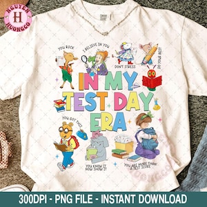 Könnte beinhalten: Weißes T-Shirt mit einem farbenfrohen Grafikdesign mit Zeichentrickfiguren und dem Text "IN MY TEST DAY ERA". Das Design enthält Sätze wie "You Rock", "I Believe in You" und "You Got This".