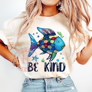 Peut inclure: Un t-shirt blanc avec un poisson bleu et violet aux écailles colorées et le texte "Be Kind" imprimé sur le devant.