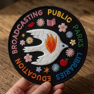 May include: Embroidered black patch with the words "Broadcasting Education Public Parks Libraries" in a circular design. The patch features a white dove with orange flames, flowers, a book, a red apple, and a red lip design.