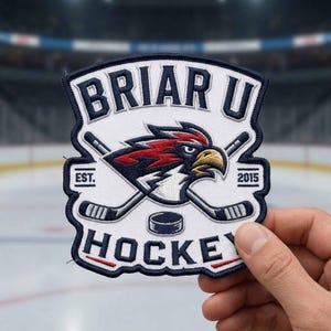 May include: Embroidered patch with the text "BRIAR U HOCKEY" and a stylized eagle head logo. The patch features crossed hockey sticks, a puck, and the year "2015". The patch has a white background with navy blue, red, and yellow accents.