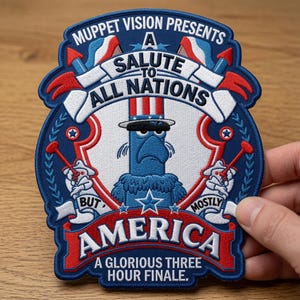 Op de afbeelding: Een blauwe, rode en witte geborduurde patch met Sam de Adelaar die een hoge hoed draagt. De tekst luidt: MUPPET VISION PRESENTS A SALUTE TO ALL NATIONS BUT MOSTLY AMERICA A GLORIOUS THREE HOUR FINALE. Het ontwerp bevat vuurwerk en sterren.