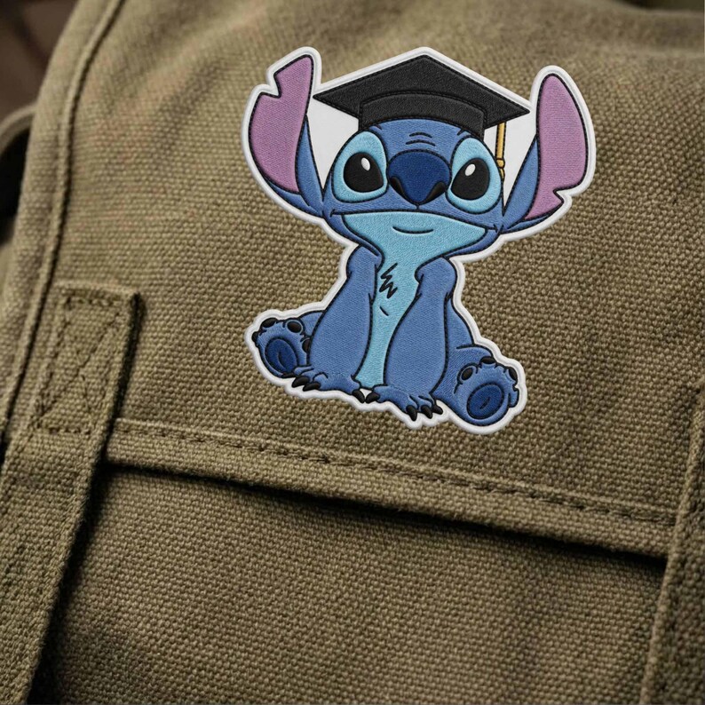 K&ouml;nnte beinhalten: Ein blau-wei&szlig;er, gestickter Aufn&auml;her mit der Figur Stitch aus Lilo & Stitch, der eine schwarze Abschlusskappe mit goldener Quaste tr&auml;gt. Der Aufn&auml;her befindet sich auf einer gr&uuml;nen Leinwandtasche.