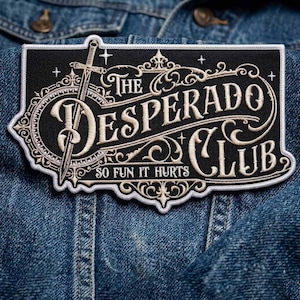 Op de afbeelding: Een rechthoekige zwarte patch met de woorden "The Desperado Club" in een sierlijk, crèmekleurig lettertype. Een zwaard is afgebeeld aan de linkerkant. De zin "So Fun It Hurts" staat onderaan. De patch is op een spijkerjas genaaid.