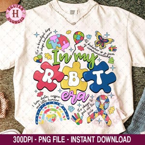 Può includere: T-shirt bianco con un design grafico colorato. Il design include pezzi di puzzle, un arcobaleno e la frase "In my RBT era". Il testo aggiuntivo include "It's a beautiful day to shape behaviors" e "All behavior is a form of communications."