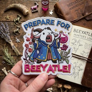May include: A white embroidered patch featuring a cartoon goat wearing a blue wizard robe with gold stars, holding a pink potion bottle. The text reads PREPARE FOR BEEYATLE! in blue and pink letters, surrounded by red flowers and small gold stars.