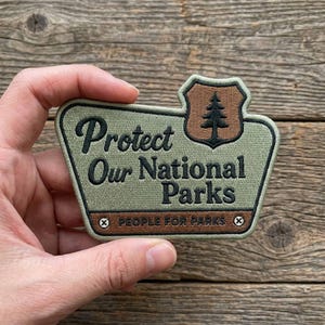 Op de afbeelding: Een groen en bruin geborduurde patch met de tekst "Protect Our National Parks". De patch heeft een schild met een boom en de tekst "People for Parks".